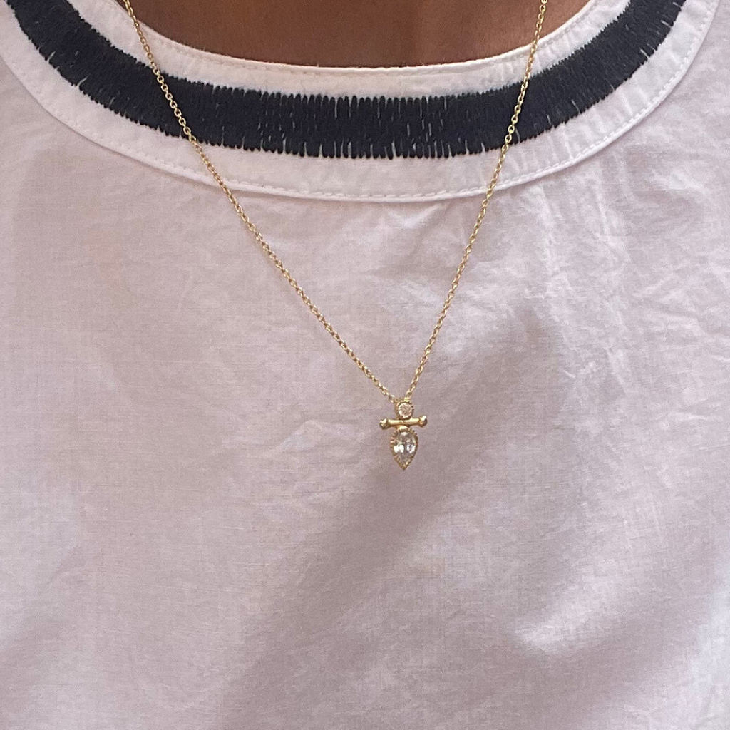 Gold necklace with a pendant on a white shirt with black trim
