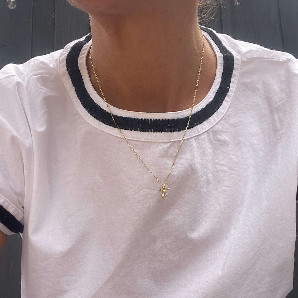 Person wearing a white shirt with black trim and a gold necklace with a pendant.