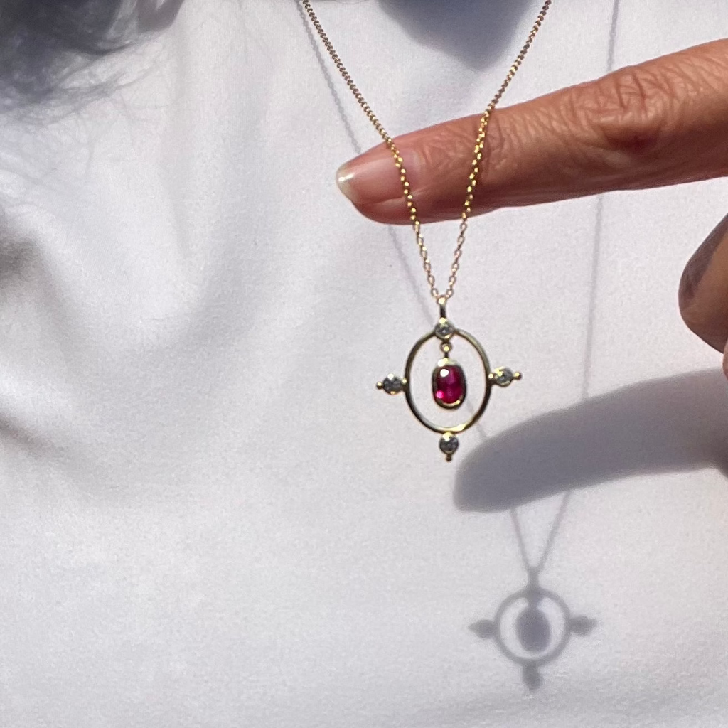 Gold necklace with a red gemstone pendant held by a hand on a white background