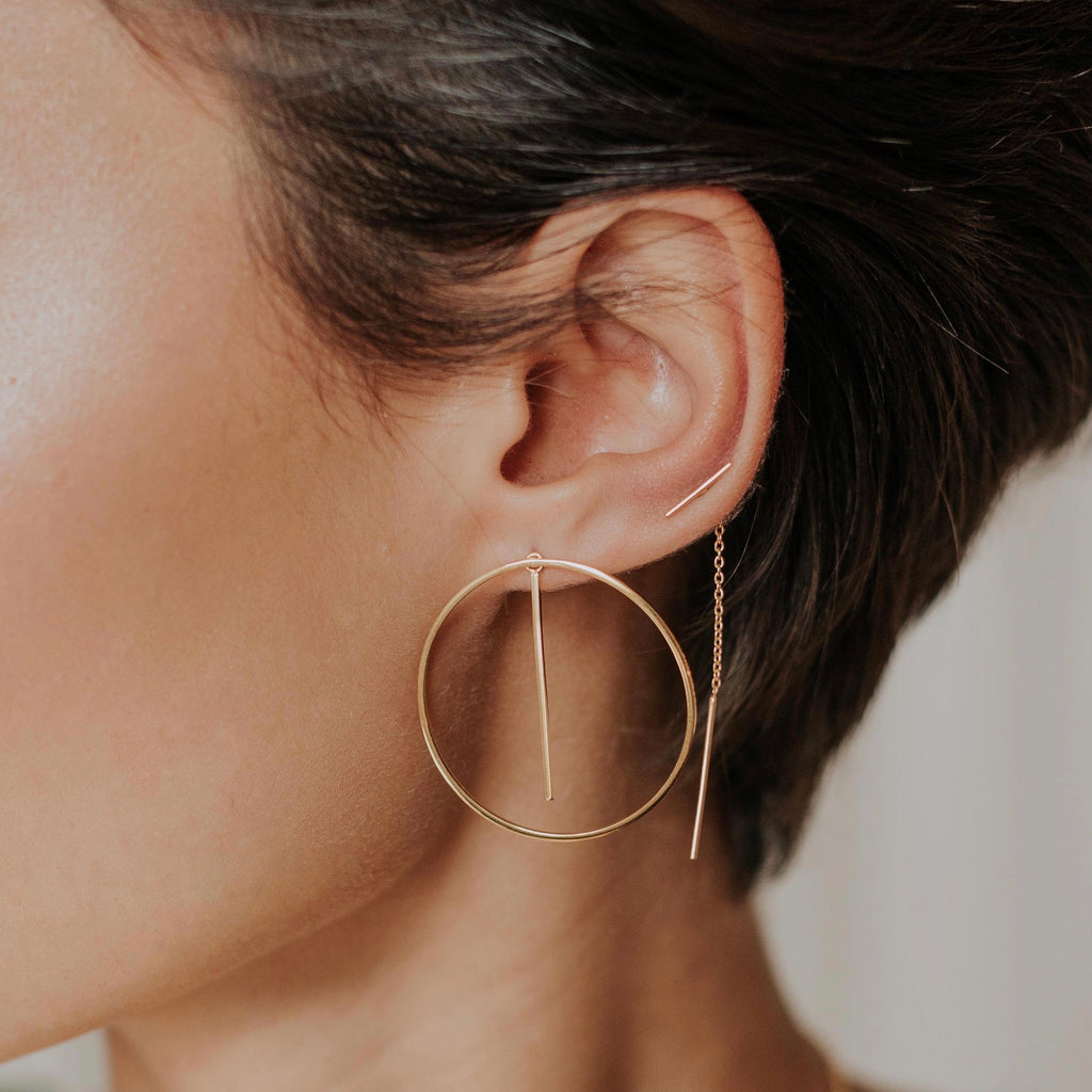 Close-up of a person wearing gold hoop earrings with a blurred background
