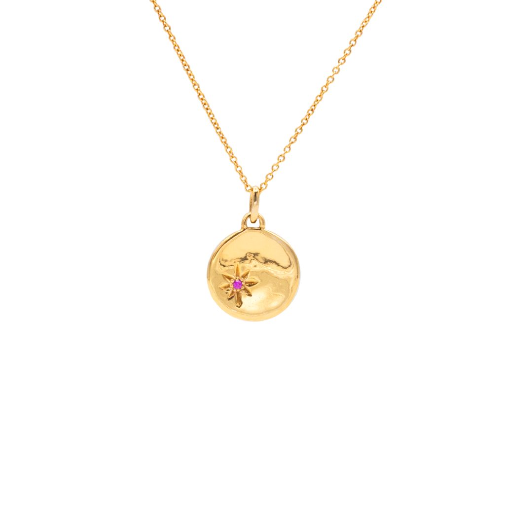 A gold-plated necklace with a round medallion pendant featuring a star-shaped created ruby, suspended from a delicate chain.