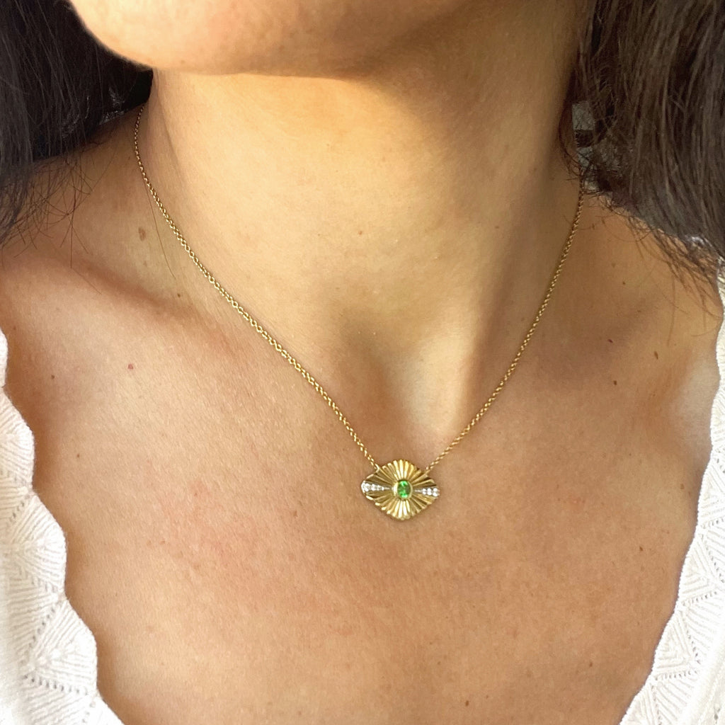 Gold necklace with a green gemstone on a person wearing a white top.